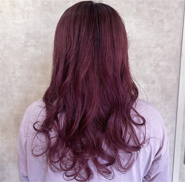 赤みのあるラベンダーカラーのロングヘア。ゆるやかなカールでツヤ感を引き立てたスタイル。