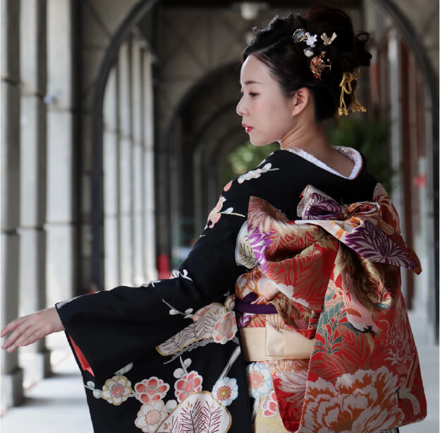 黒地の振袖に華やかな帯を合わせた和装ヘアスタイル。上品なまとめ髪に金の髪飾りを添えた仕上がり。